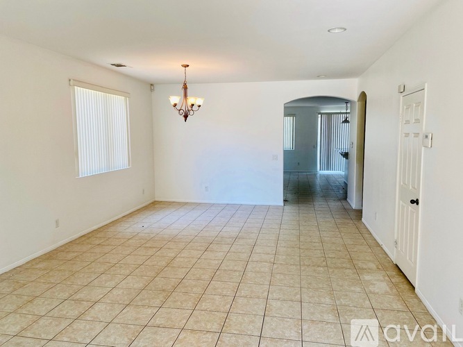 A room with a chandelier, tiled floor, and a door leading to a hallway.