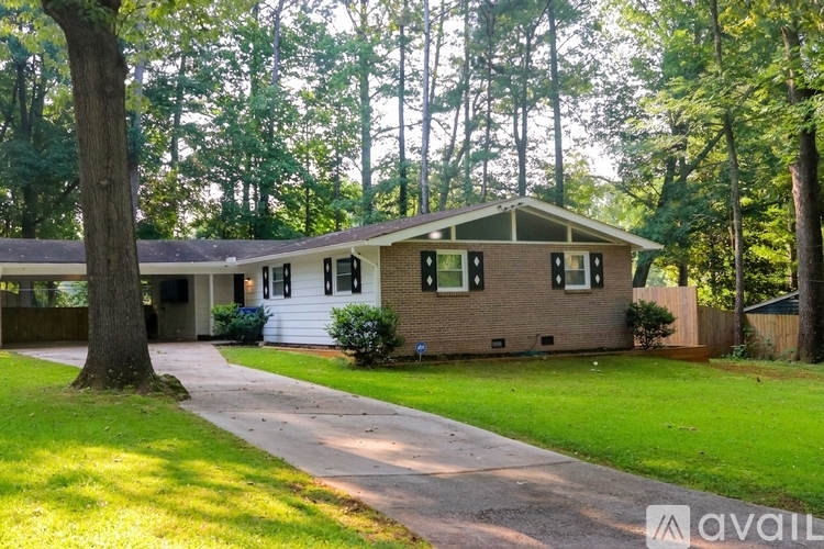 A house with a brown roof and white trim is surrounded by a green lawn and trees.