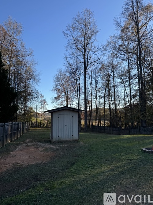 A small building sits in the middle of a field with a fence and trees in the background.