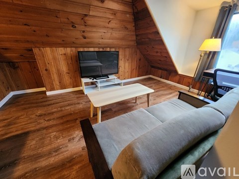 A living room with a couch, a television, and a wooden wall.