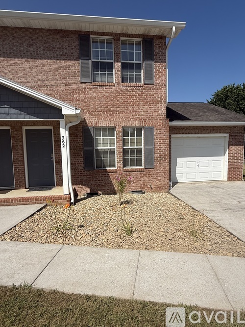 A brick house with a white garage door and a small tree in front.