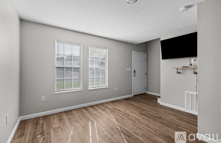 A spacious room with wooden flooring and two windows.