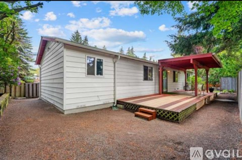 A mobile home with a red awning is surrounded by trees and has a gravel driveway.