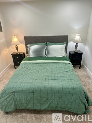 A bed with a green comforter and two pillows sits in a room with two lamps on either side.