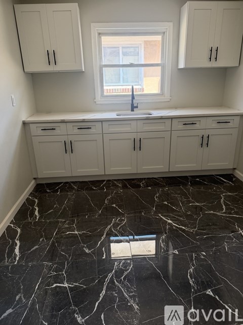 A kitchen with white cabinets and a marble floor.