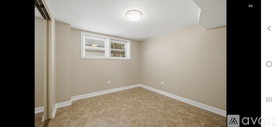 A room with beige walls and carpeting, a window with white blinds, and a ceiling light.