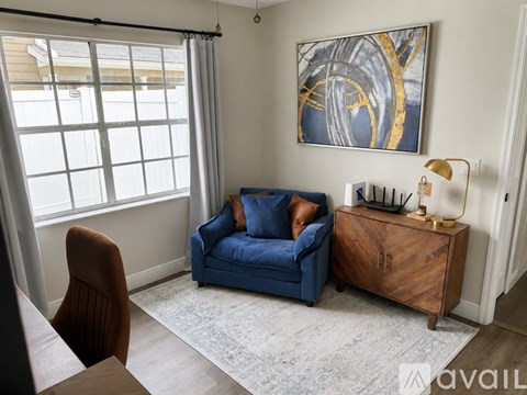 A blue couch sits in a living room with a painting on the wall and a wooden cabinet.