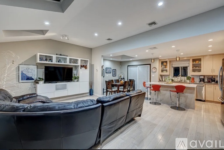 A modern living room with a black sofa and a kitchen area in the background.