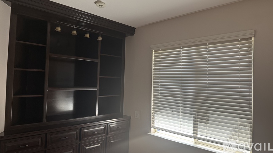 A room with a dark brown cabinet and a window with white blinds.