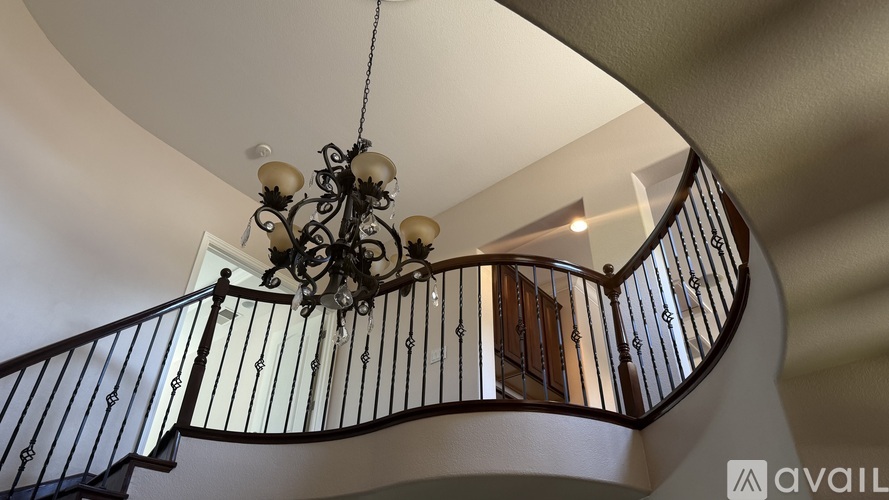 A chandelier hangs from the ceiling above a staircase with a black railing.