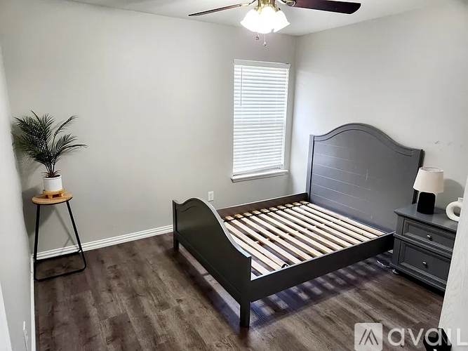 A bedroom with a bed, nightstand, and plant.