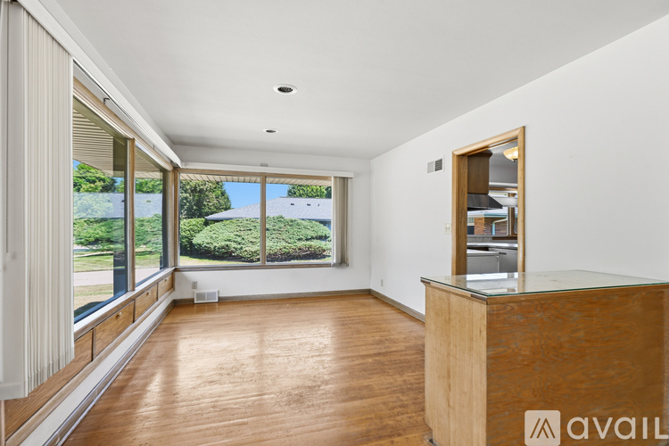 A spacious room with wooden floors and a large window overlooking a garden.