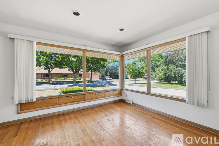 A room with wooden floors and large windows with a view of a street and trees.