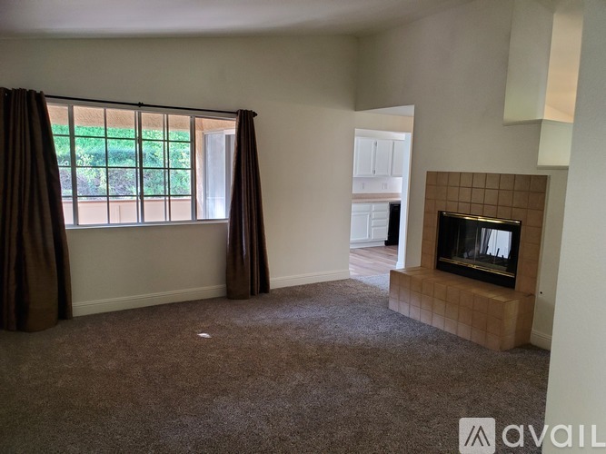 A living room with a fireplace and a window with curtains.