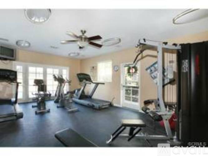 A well-equipped gym with various exercise machines and a fan on the ceiling.