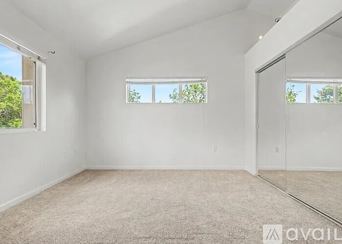 A spacious room with a carpeted floor, two windows, and a sliding glass door.
