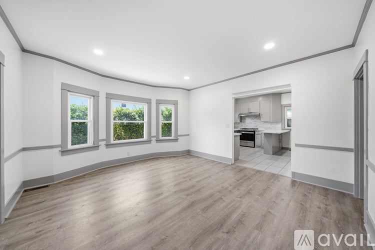 A spacious room with wooden flooring and three windows.