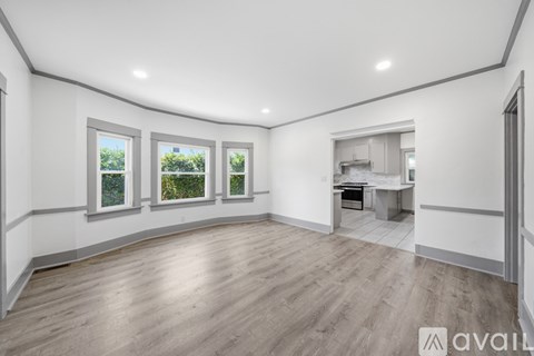 A spacious room with wooden flooring and three windows.