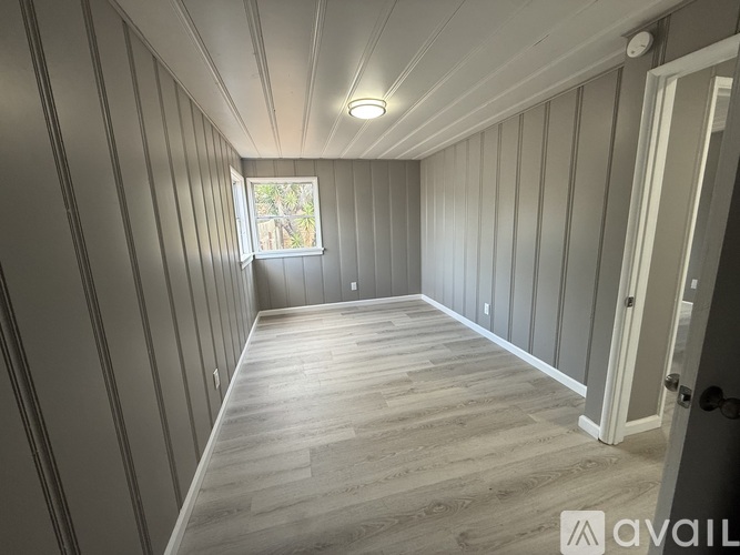 A room with wooden floors and walls, a window, and a door.