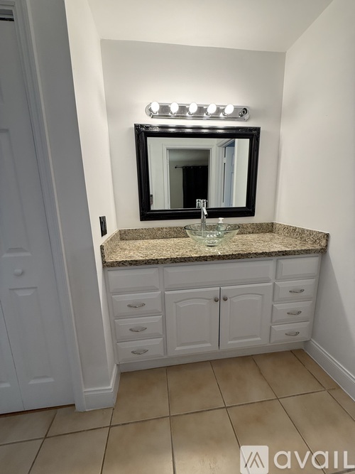 A bathroom with a granite countertop and a mirror with lights above it.