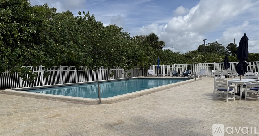 A pool surrounded by trees and chairs with an umbrella.