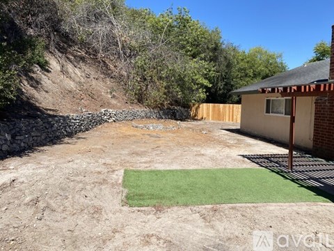 A backyard with a small patch of grass and a house in the background.