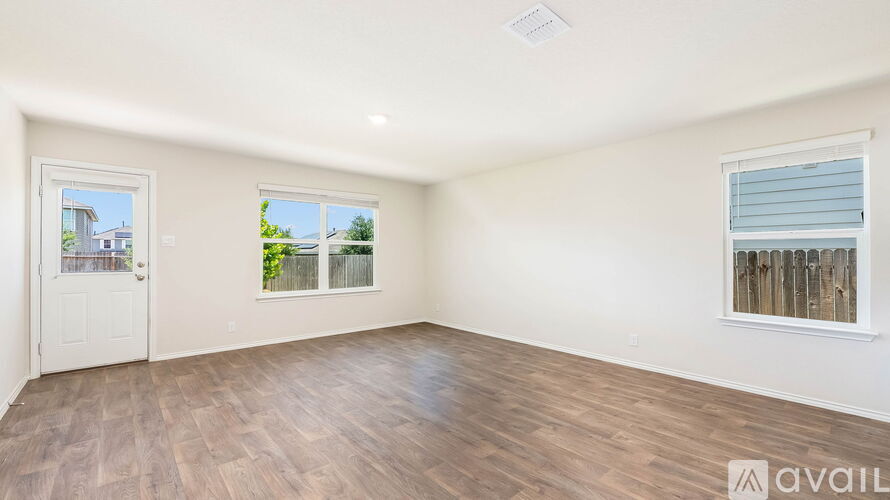 A spacious room with wooden flooring and two windows.