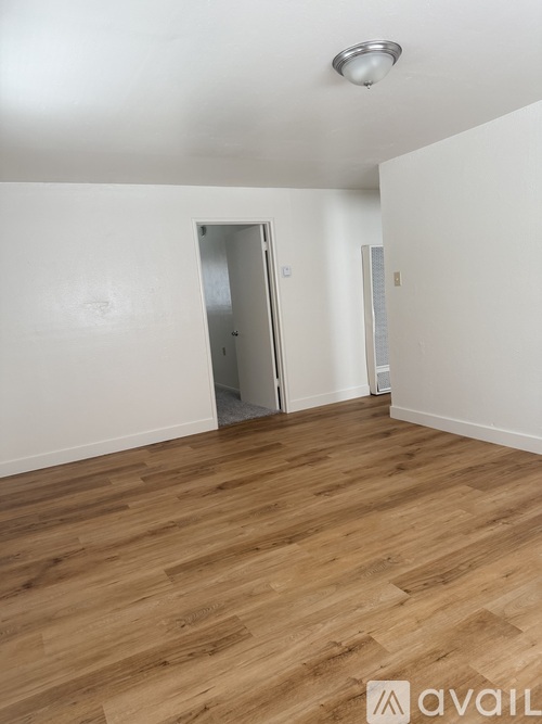 A room with wooden flooring and a white wall with a door.