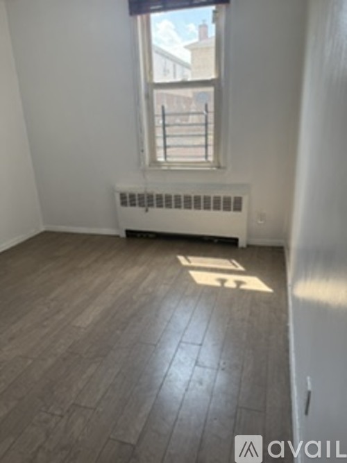 A room with wooden flooring and a window with a view of a building outside.