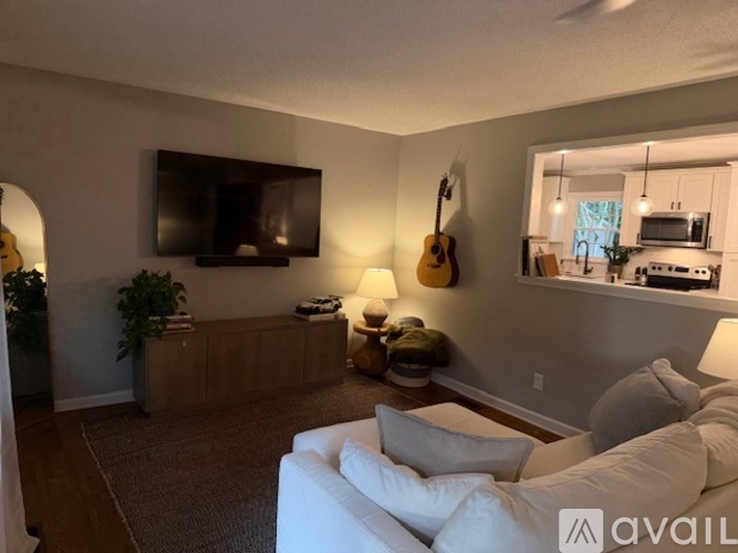 A living room with a white couch and a guitar hanging on the wall.