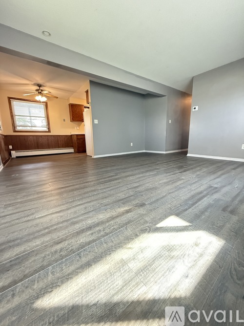 A spacious room with wooden flooring and a window on the left wall.