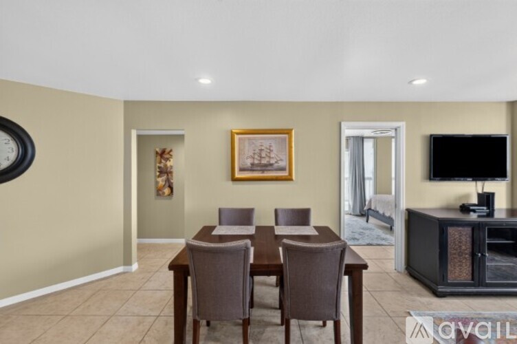 A dining room with a wooden table and chairs, a television, and a painting on the wall.