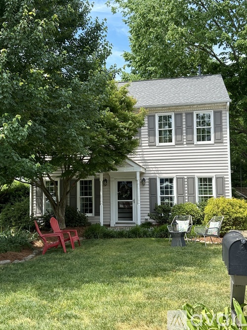 A house with a grey roof and white siding is surrounded by greenery.