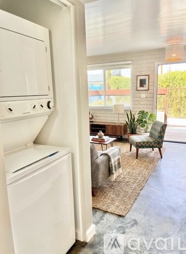 A white kitchen with a washing machine and a chair in the living room.