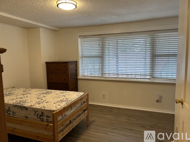 A bedroom with a bed, dresser, and window with blinds.