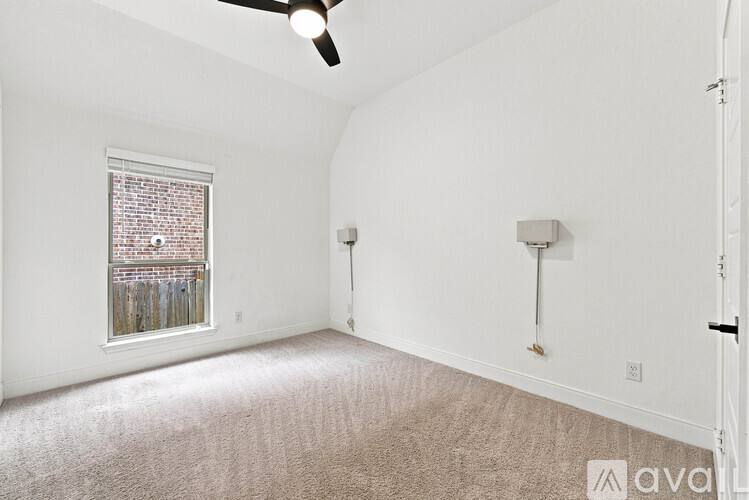 A room with a carpeted floor, a ceiling fan, and a window with a view of a fence and a building.