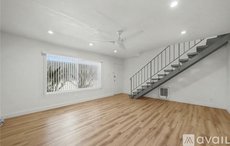 A spacious room with wooden flooring and a staircase.