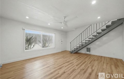 A spacious room with wooden flooring and a staircase.