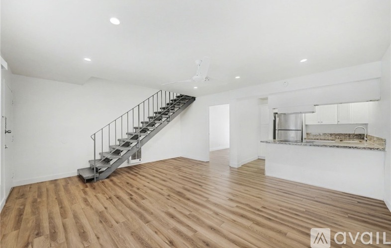 A spacious room with wooden flooring and a staircase.