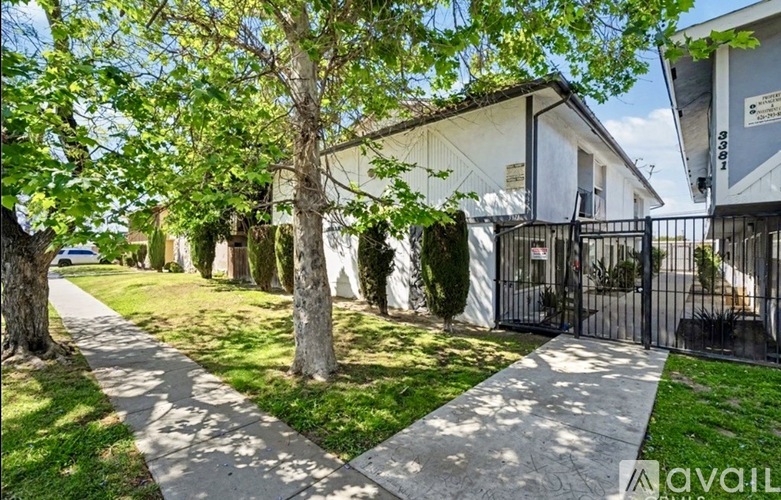 A white house with a black gate and a tree in front.