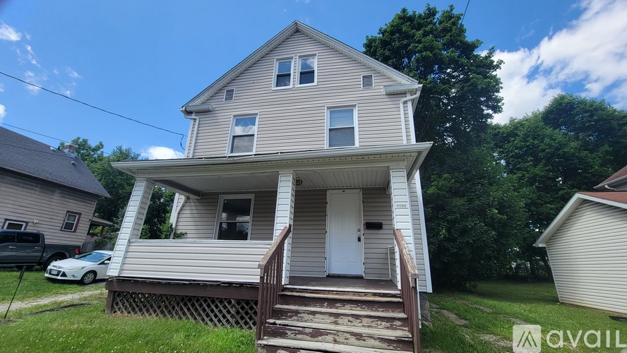A two-story house with a porch and a car parked in the driveway.