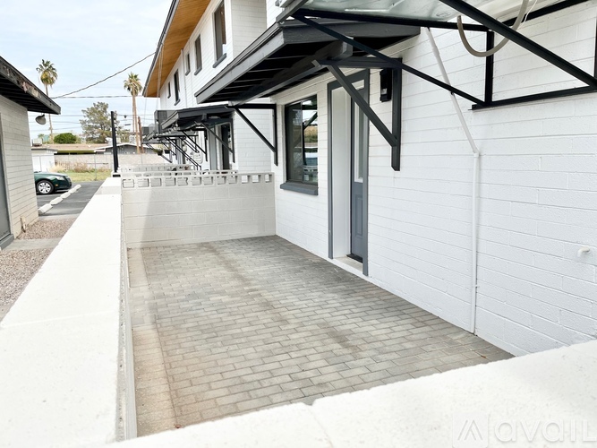 A white building with a black awning and a brick walkway.