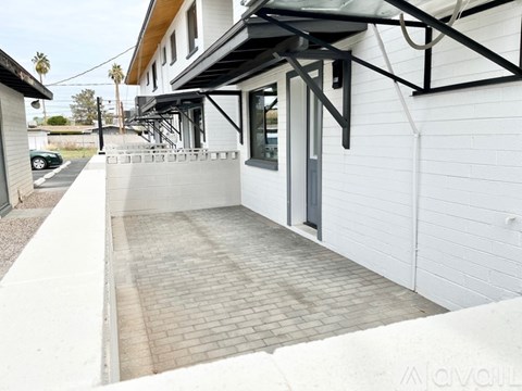 A white building with a black awning and a brick walkway.