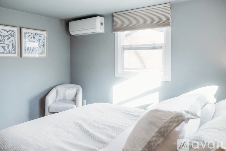 A bedroom with a white bed and a window with blinds.