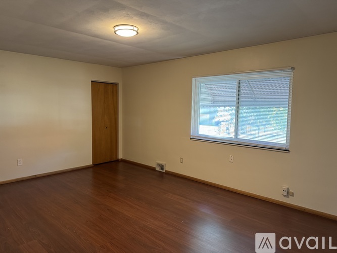 A room with a wooden floor and a window with blinds.