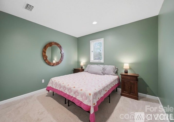 A bedroom with a bed, nightstand, and a mirror on the wall.