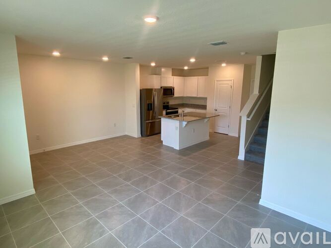A spacious kitchen with a tiled floor and a staircase in the background.