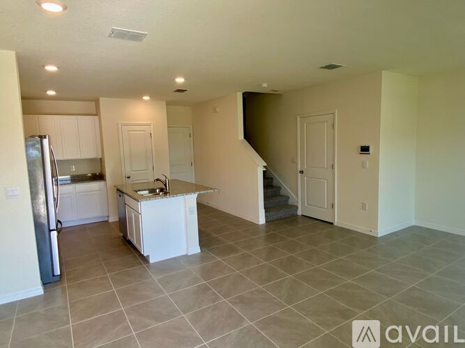 A kitchen with a refrigerator, sink, and stairs in the background.