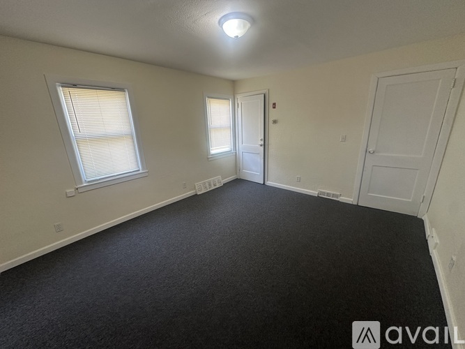 A room with a carpeted floor, two doors, and two windows.