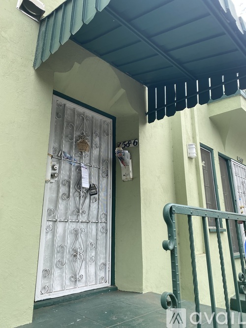 A white door with a metal grill is on a yellow building.